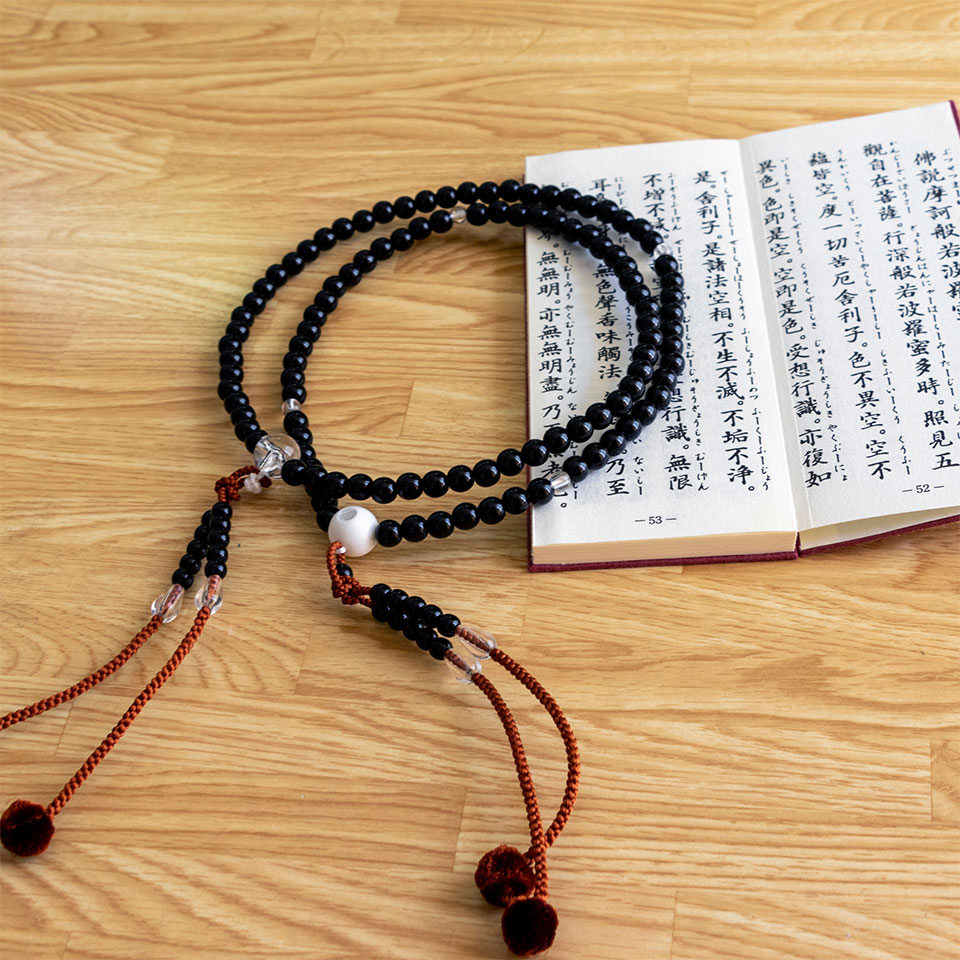 Black prayer beads with red tassels lying on a wooden surface next to an open book with Chinese text