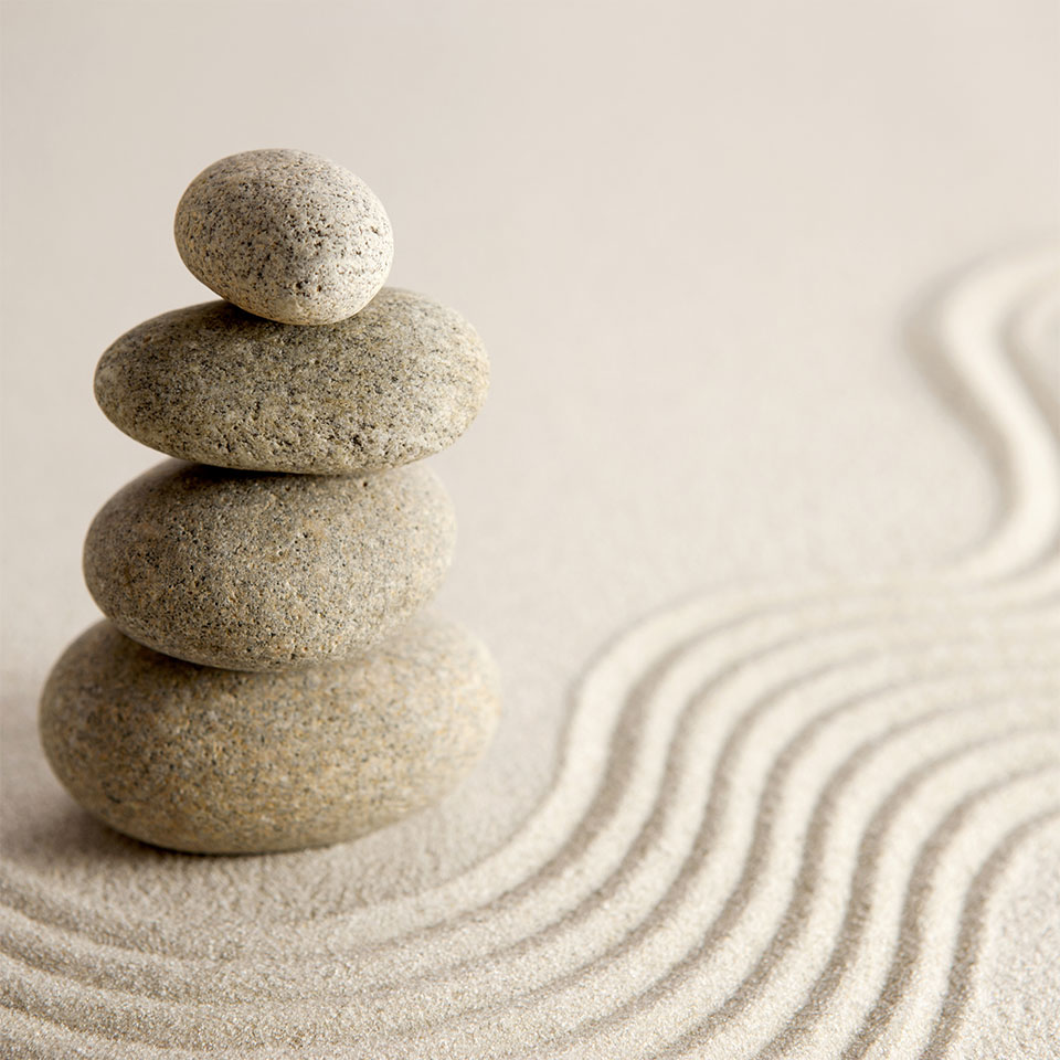 Four smooth stones stacked in a balanced tower on raked sand with circular patterns