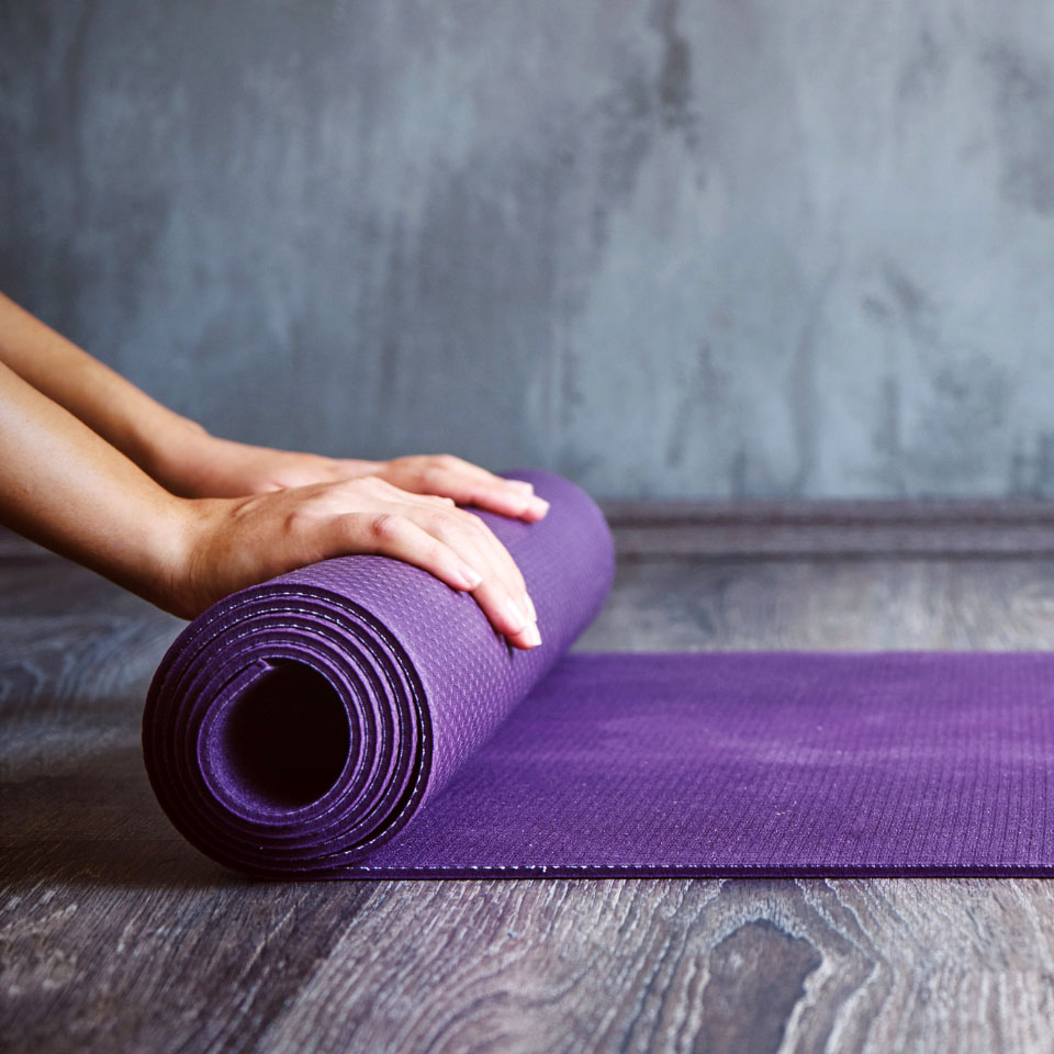Hands resting on a rolled up purple yoga mat